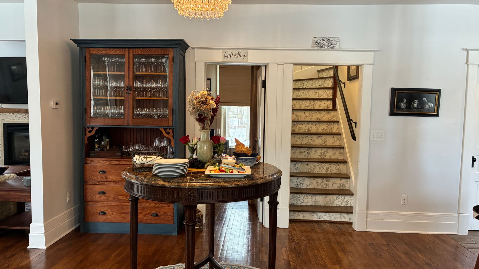 A cozy dining area featuring a round table with food, an antique cabinet, and a staircase in the background.